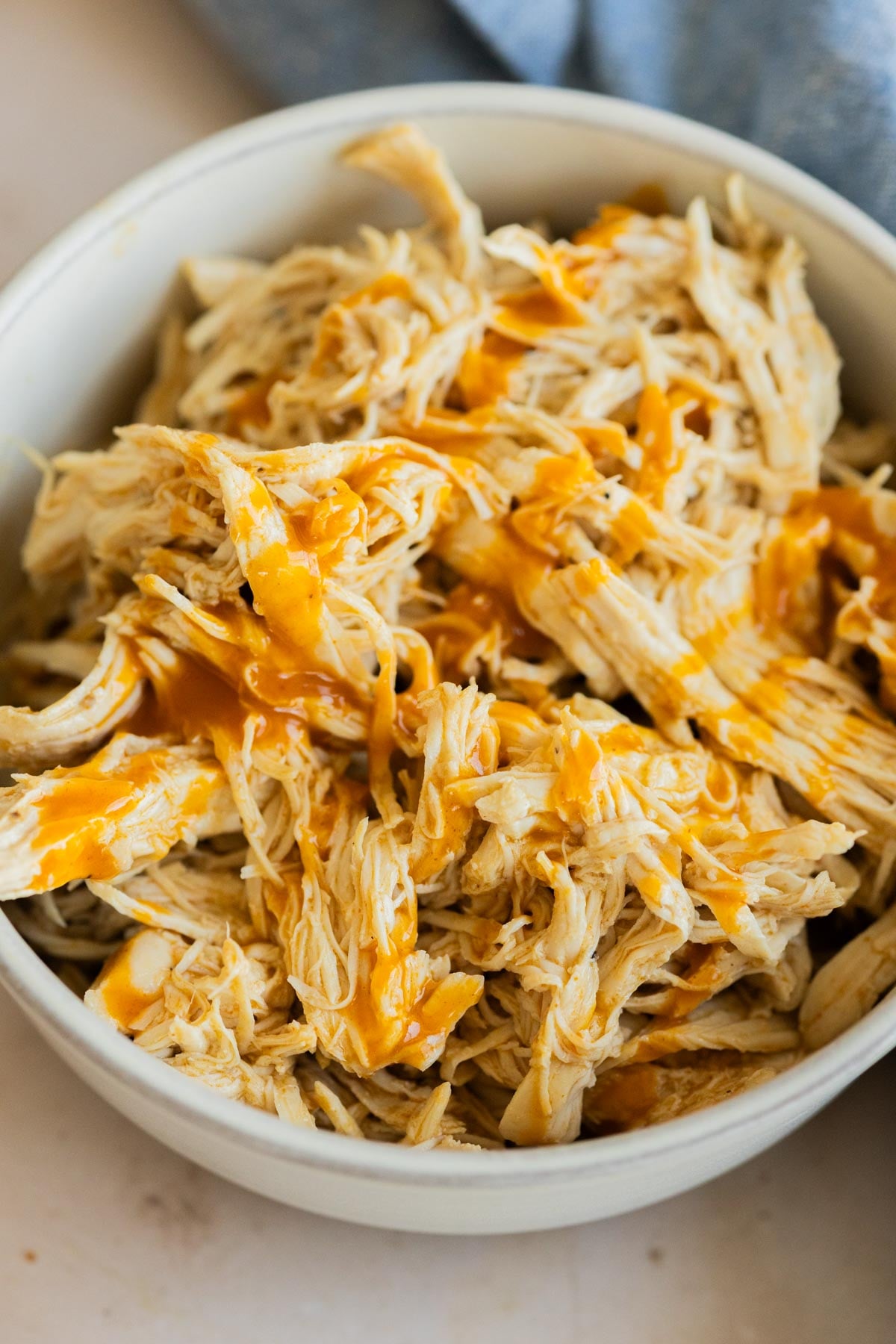 Instant Pot buffalo chicken in a grey bowl. Next to a blue cloth on a table.