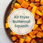 A plate of roasted air fryer butternut squash cubes garnished with herbs, with text overlay reading "Air Fryer Butternut Squash.