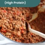 A pot of hearty beanless chili with ground meat, red bell peppers, and tomato sauce is being stirred with a wooden spoon.