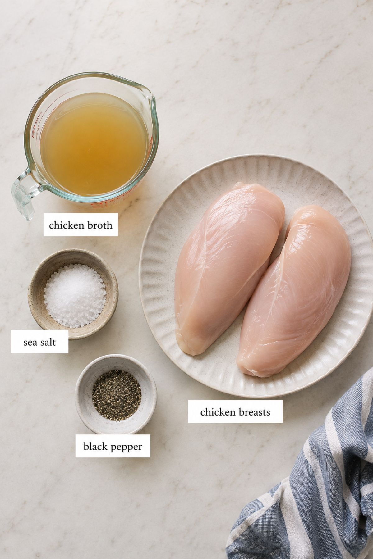 Two raw chicken breasts on a plate, a measuring cup of chicken broth, and small bowls of sea salt and black pepper are arranged on a marble surface—perfectly prepped for making Instant Pot shredded chicken.