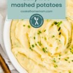 A bowl of creamy dairy free mashed potatoes garnished with chopped chives, a wooden spoon beside it, and a label reading "dairy free mashed potatoes cookathomemom.com.