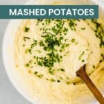 Bowl of creamy dairy free mashed potatoes topped with chopped chives, with a wooden spoon resting inside the bowl.