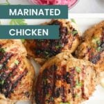 Grilled greek yogurt marinated chicken thighs garnished with herbs on a white tray, labeled “Greek Yogurt Marinated Chicken,” with a bowl of sliced pickled onions in the background.