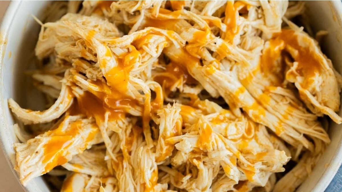 Shredded cooked chicken in a bowl, topped with a drizzle of orange-colored sauce.