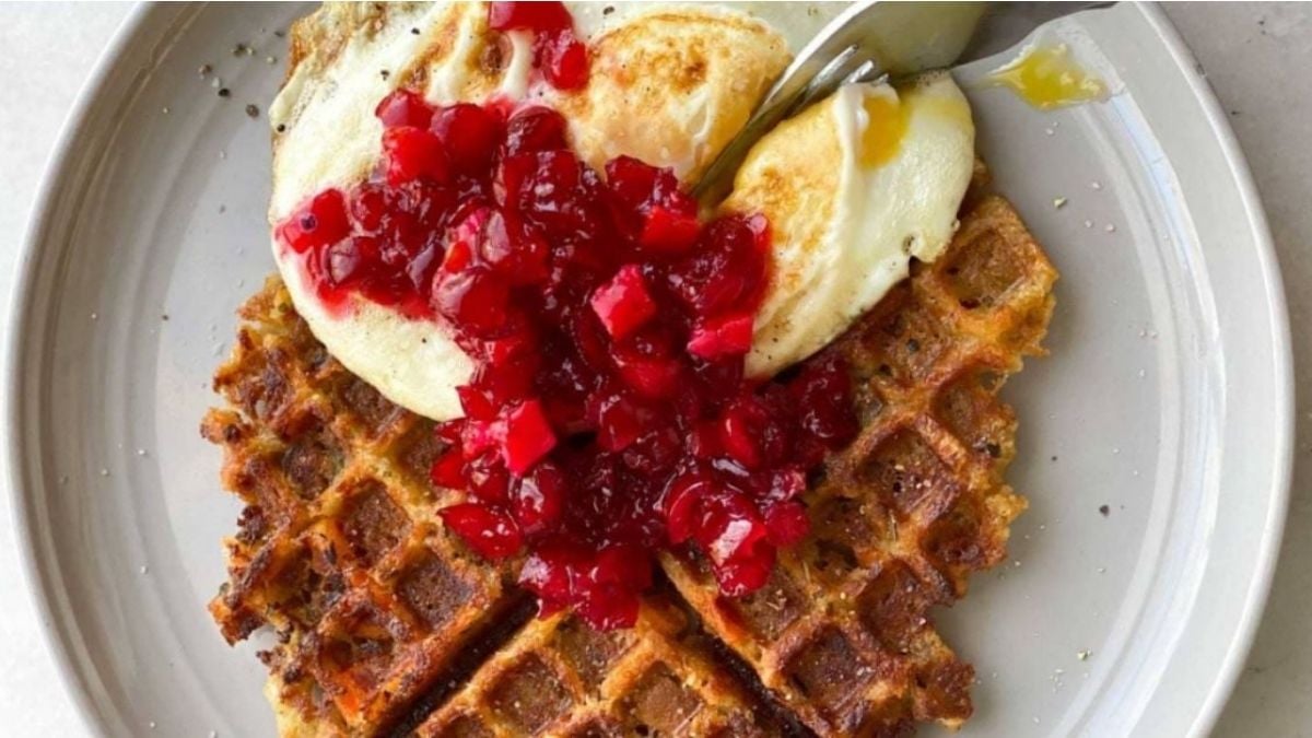 A plate with two square waffles topped with a fried egg and a generous spoonful of cranberry compote.