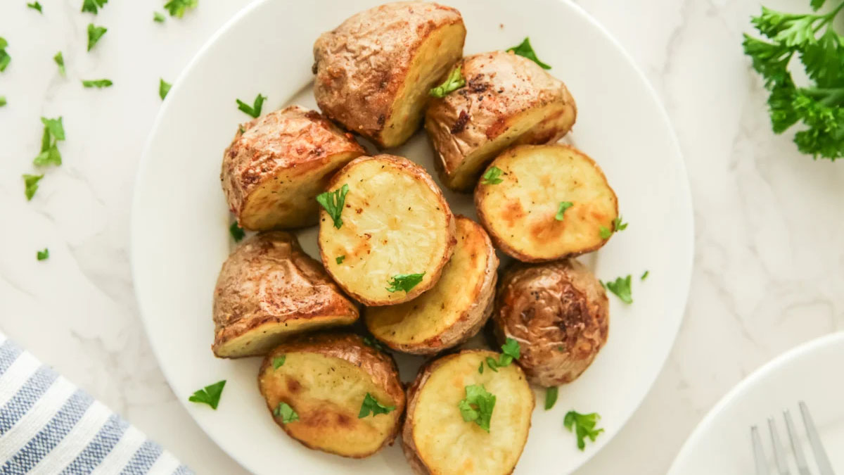 A white plate with roasted potato halves garnished with chopped parsley, placed on a light-colored surface—one of the perfect lighter holiday sides for your festive table.