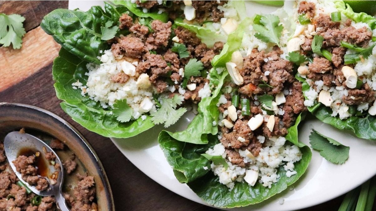 Romaine lettuce leaves filled with ground meat, cauliflower rice, chopped nuts, herbs, and green onions arranged on a plate.