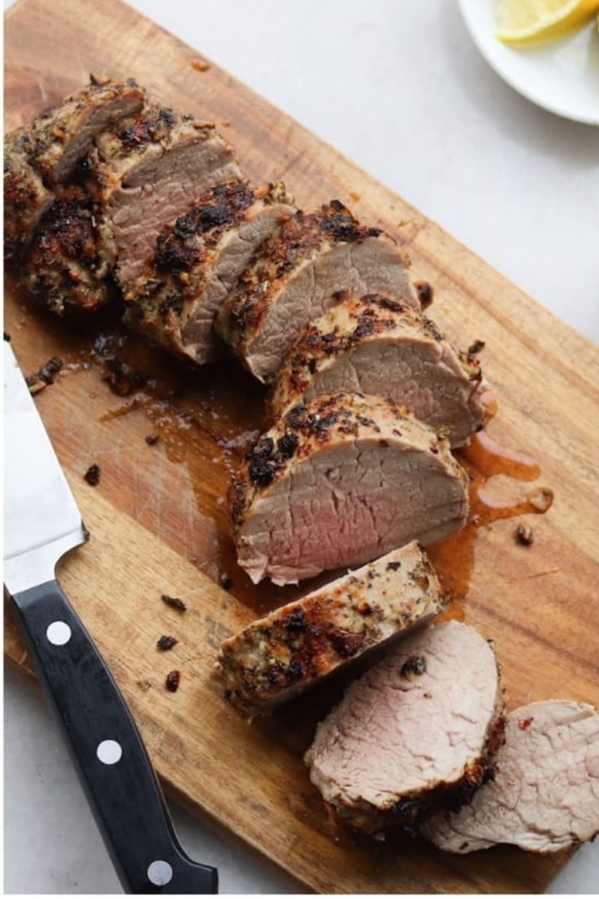 Slices of Italian pork tenderloin on a wooden cutting board with a chef’s knife beside it.