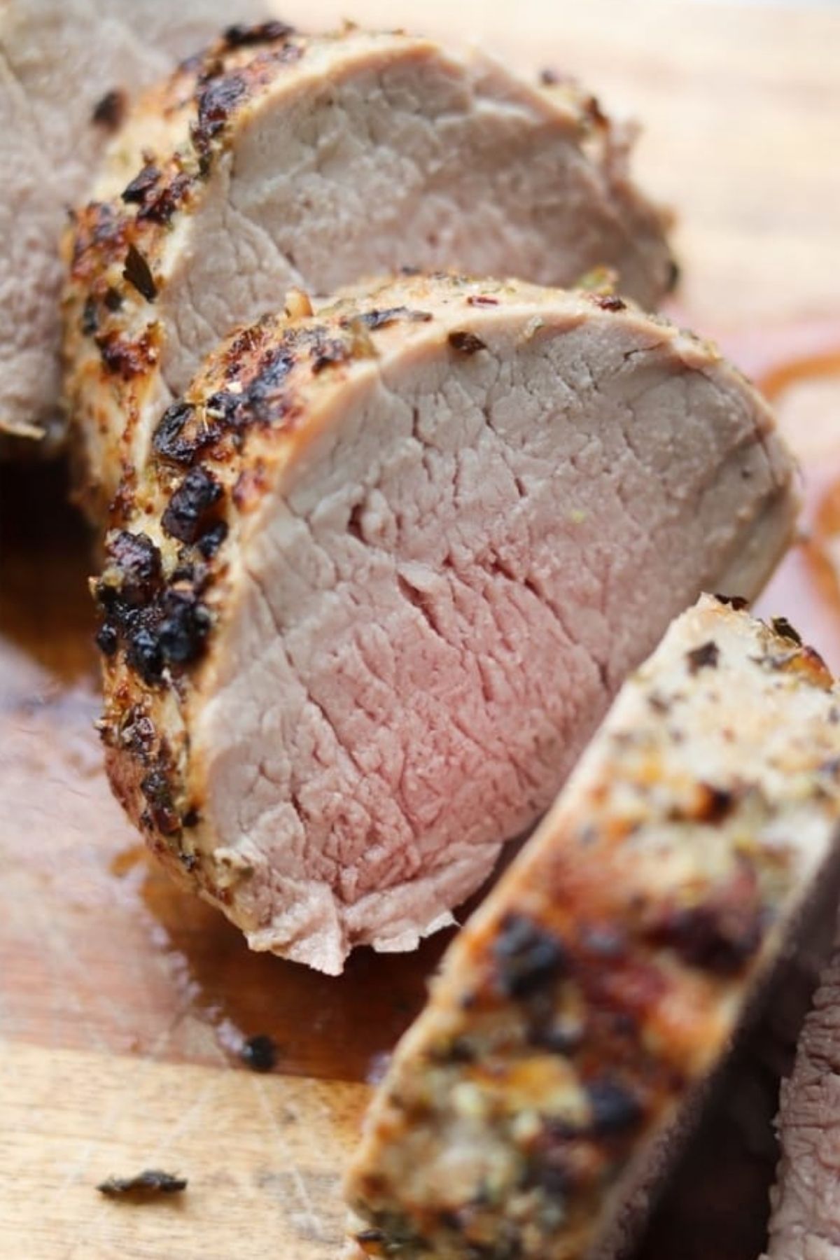 Close-up of pork tenderloin, sliced and seasoned on a wooden cutting board, highlighting the cooked exterior and slightly pink interior.