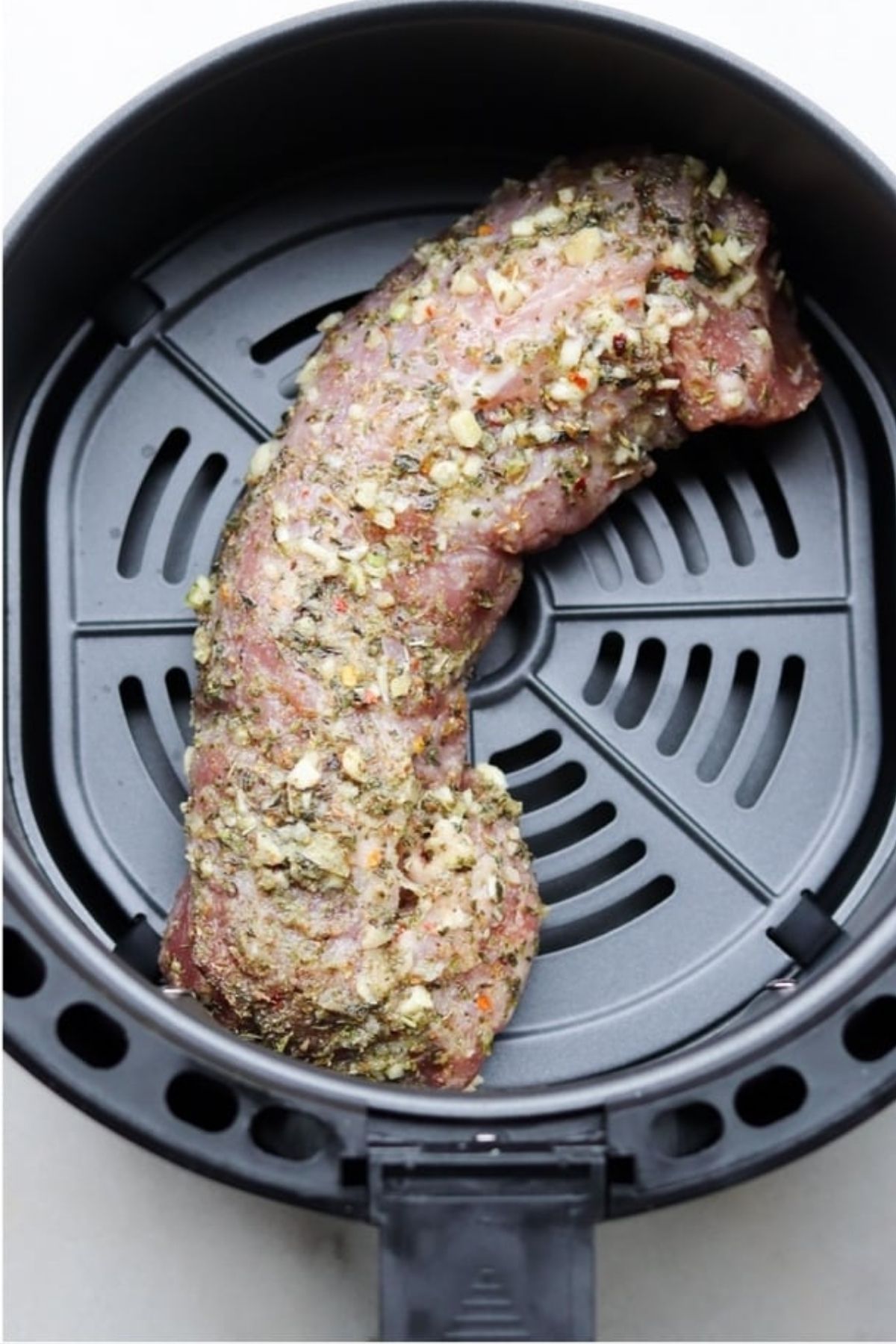 Uncooked and seasoned pork tenderloin in air fryer basket.