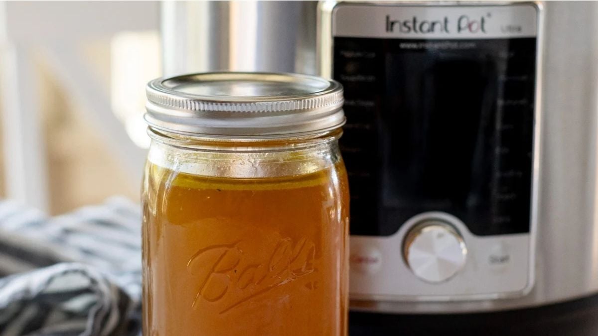A glass jar filled with broth sits in front of an Instant Pot electric pressure cooker on a kitchen counter.