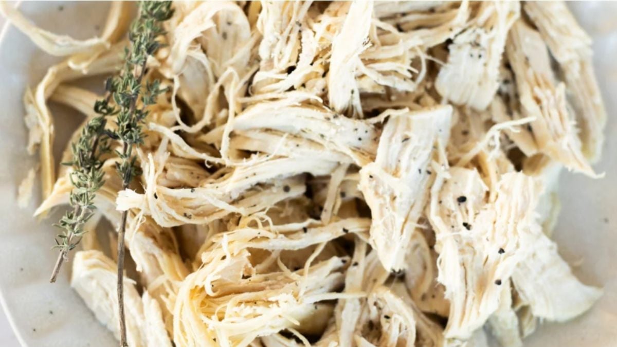 A plate of shredded cooked chicken breast garnished with sprigs of fresh thyme and sprinkled with black pepper.