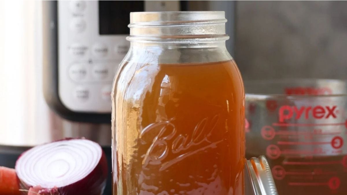A mason jar filled with brown liquid sits on a counter near a halved red onion, a Pyrex measuring cup, and an Instant Pot.