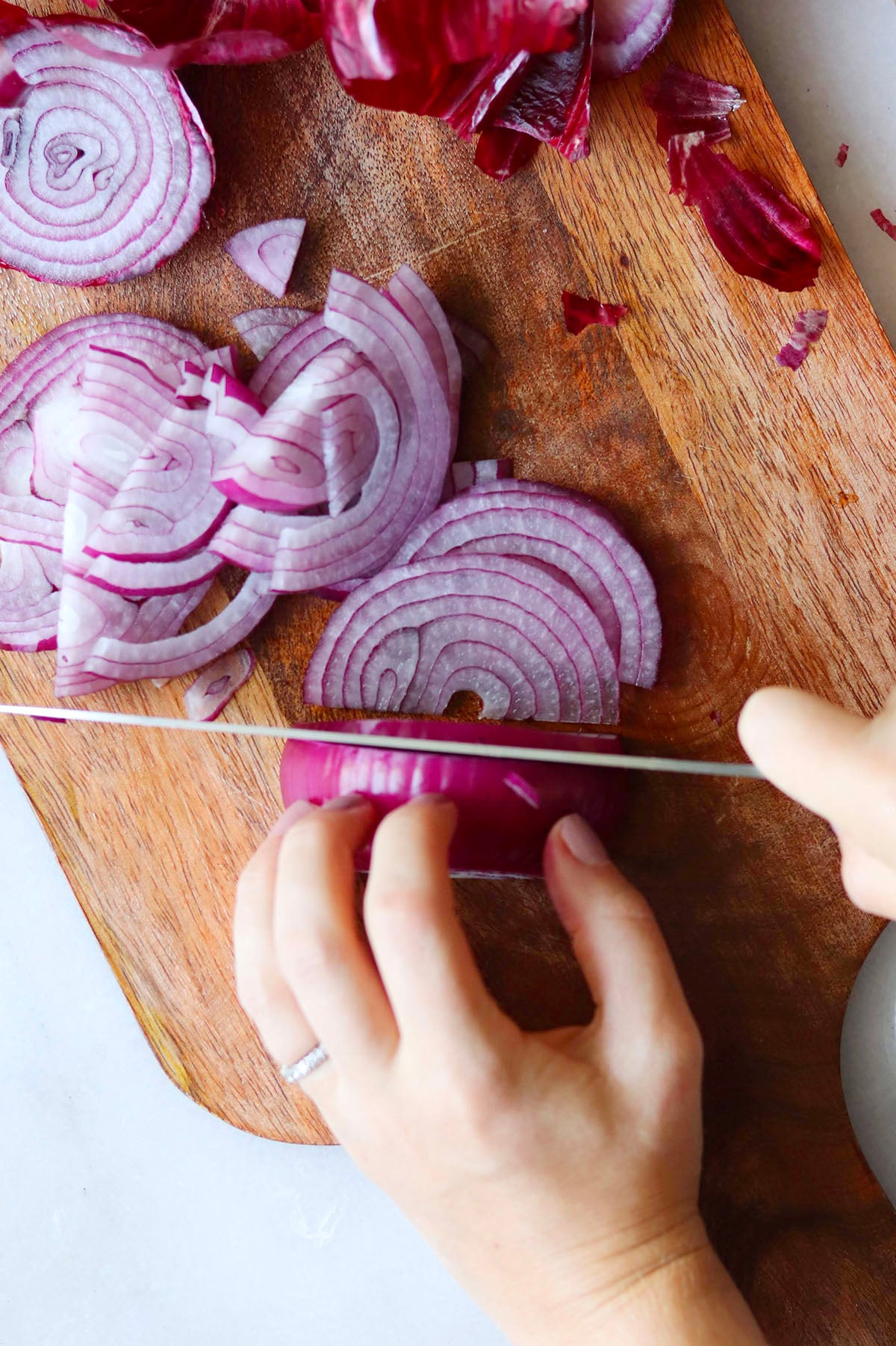 A person slices a red onion on a wooden cutting board with a chef's knife.