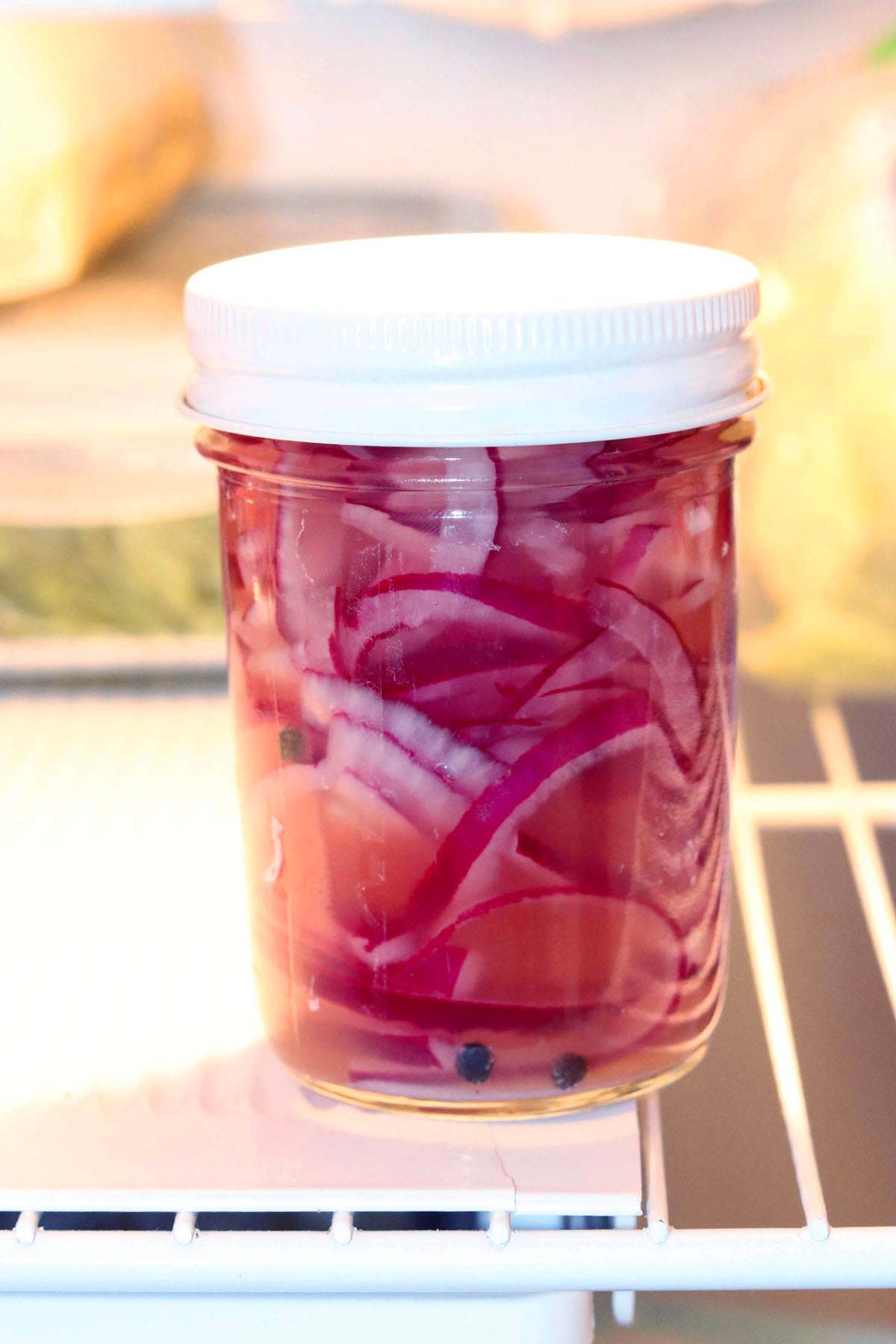 Quick pickled onions in a covered glass jar, sitting on a refrigerator shelf.