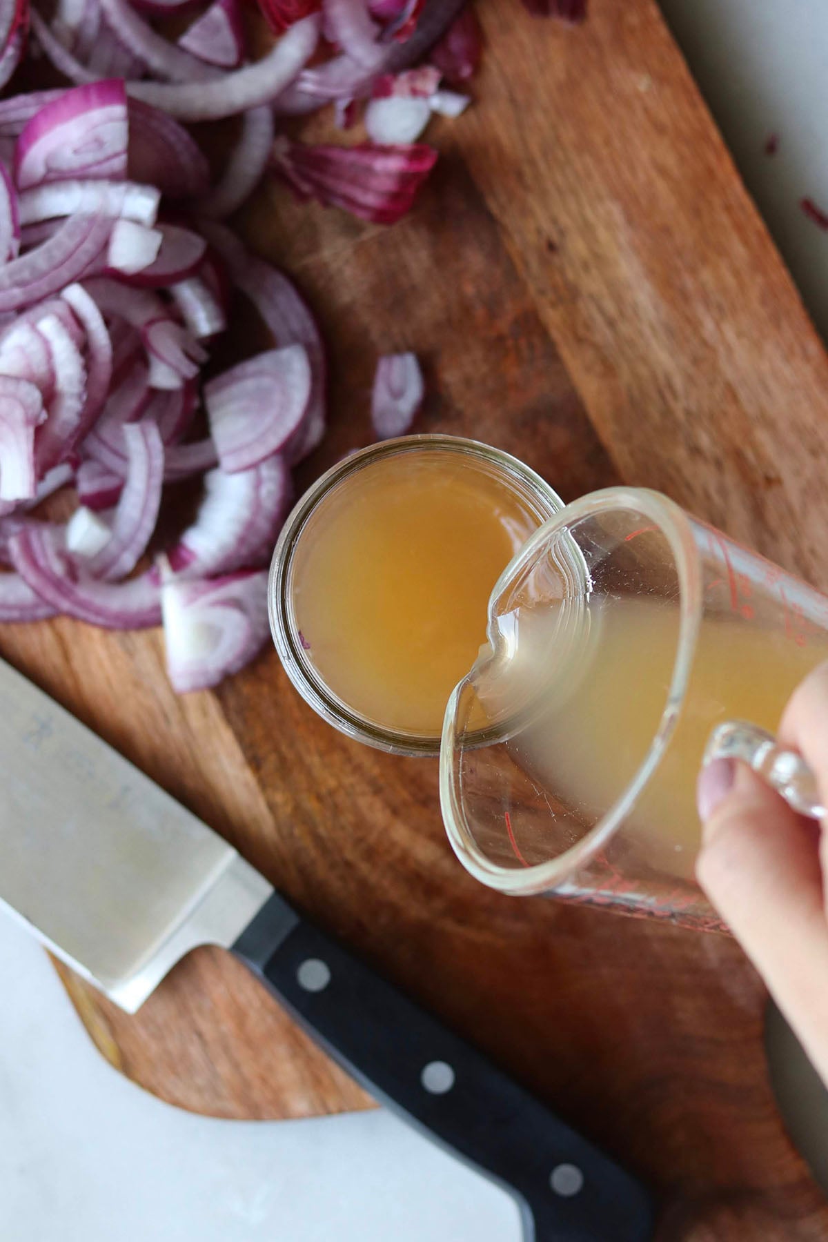 A hand pours brine from a measuring cup into a small mason jar sitting on a cutting board.