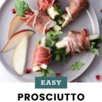 A plate with prosciutto-wrapped pear slices, arugula, and pomegranate seeds, garnished with apple slices. Text reads “Easy Prosciutto Wrapped Pears, cookathomemom.”.