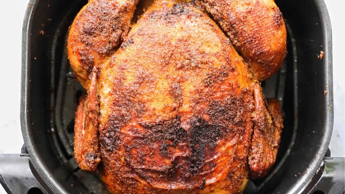 A whole cooked rotisserie-style chicken with seasoned, crispy skin sits in an air fryer basket.
