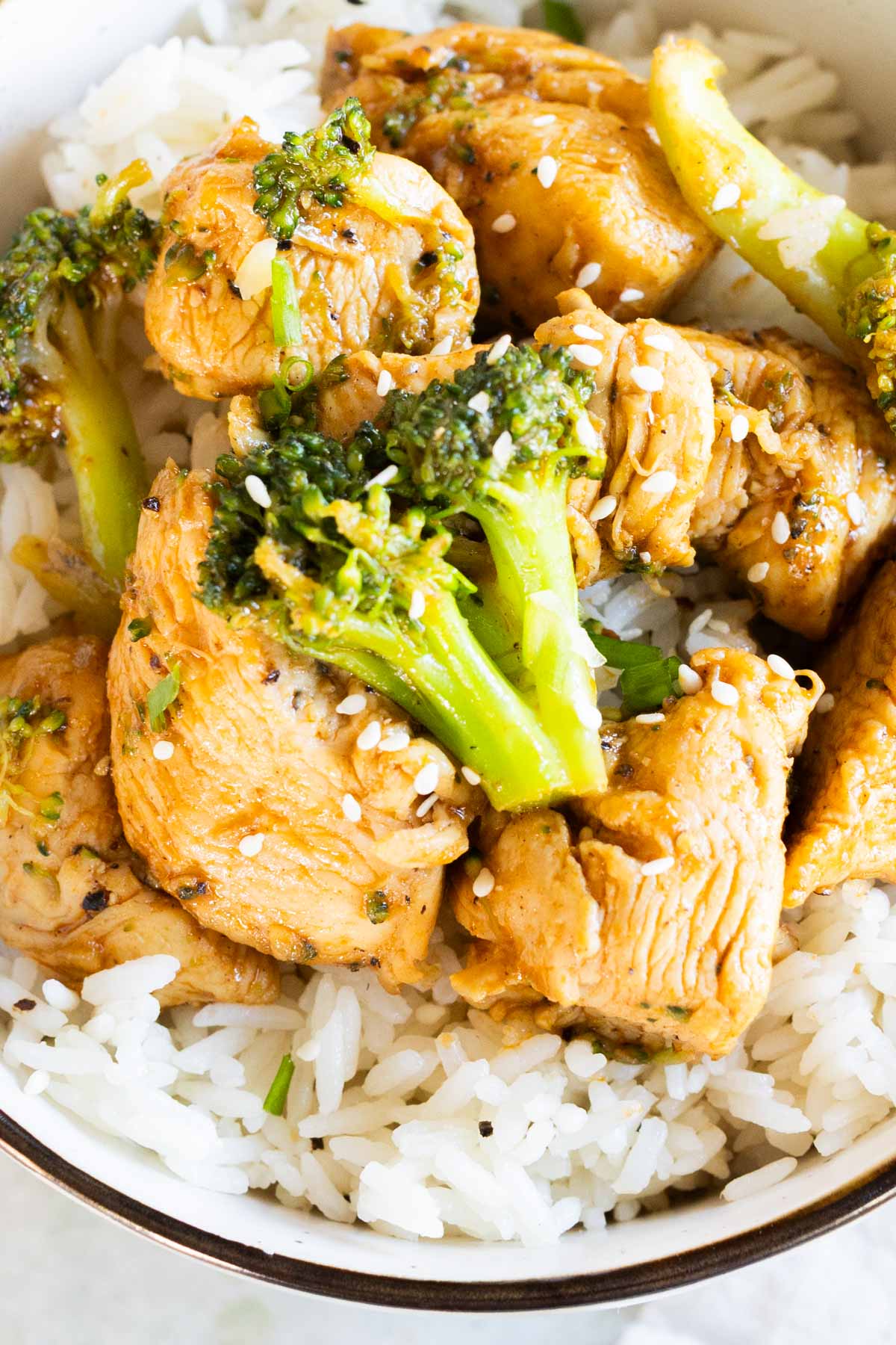 Overhead view of Chinese chicken and broccoli over cooked white rice, garnished with sesame seeds.