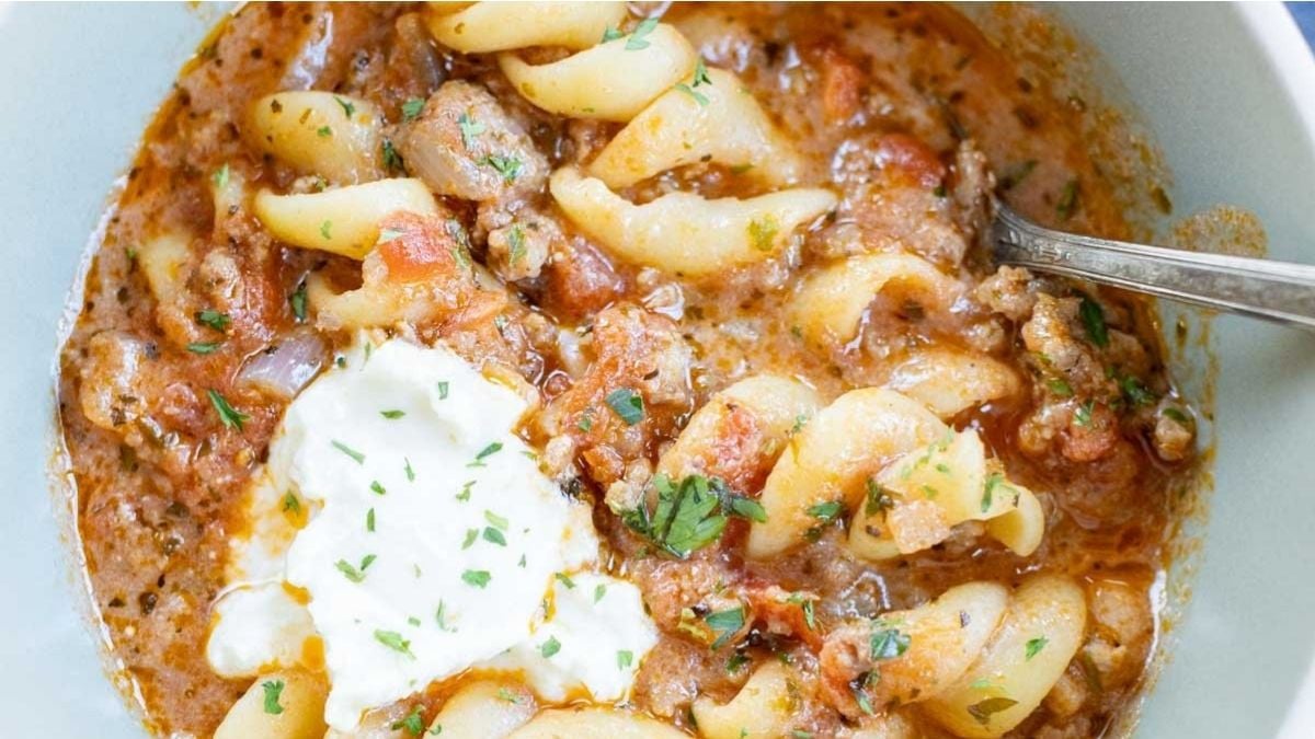 Lasagna soup in a bowl with ground meat, tomato sauce, herbs, and a dollop of sour cream, plus a spoon