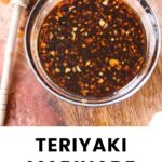 A glass bowl filled with teriyaki marinade sits on a wooden surface next to a honey dipper.