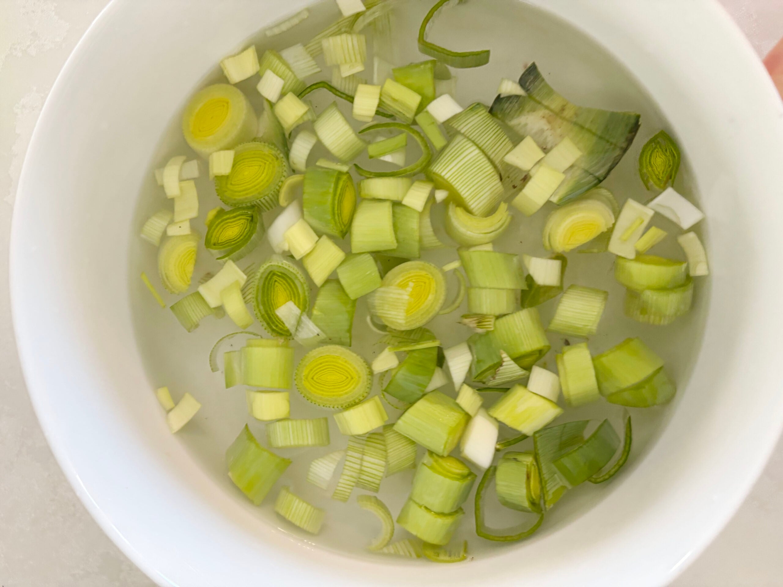 A white bowl filled with chopped leeks soaking in water.