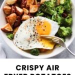 A bowl with crispy air fryer potatoes, steamed broccoli, and a sunny side up egg, garnished with black pepper and sesame seeds.