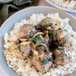 Salisbury steak meatballs, onions, herbs, and sauce served over white rice on a gray plate, with a green cloth napkin in the background.