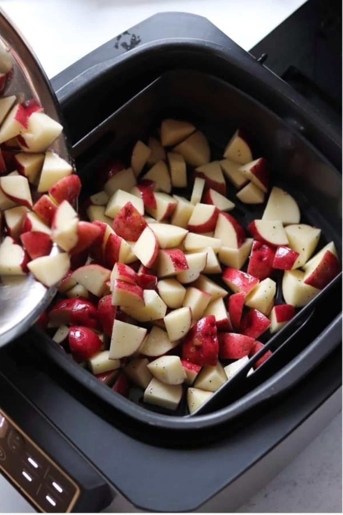Chopped red potatoes are being poured into an air fryer basket.