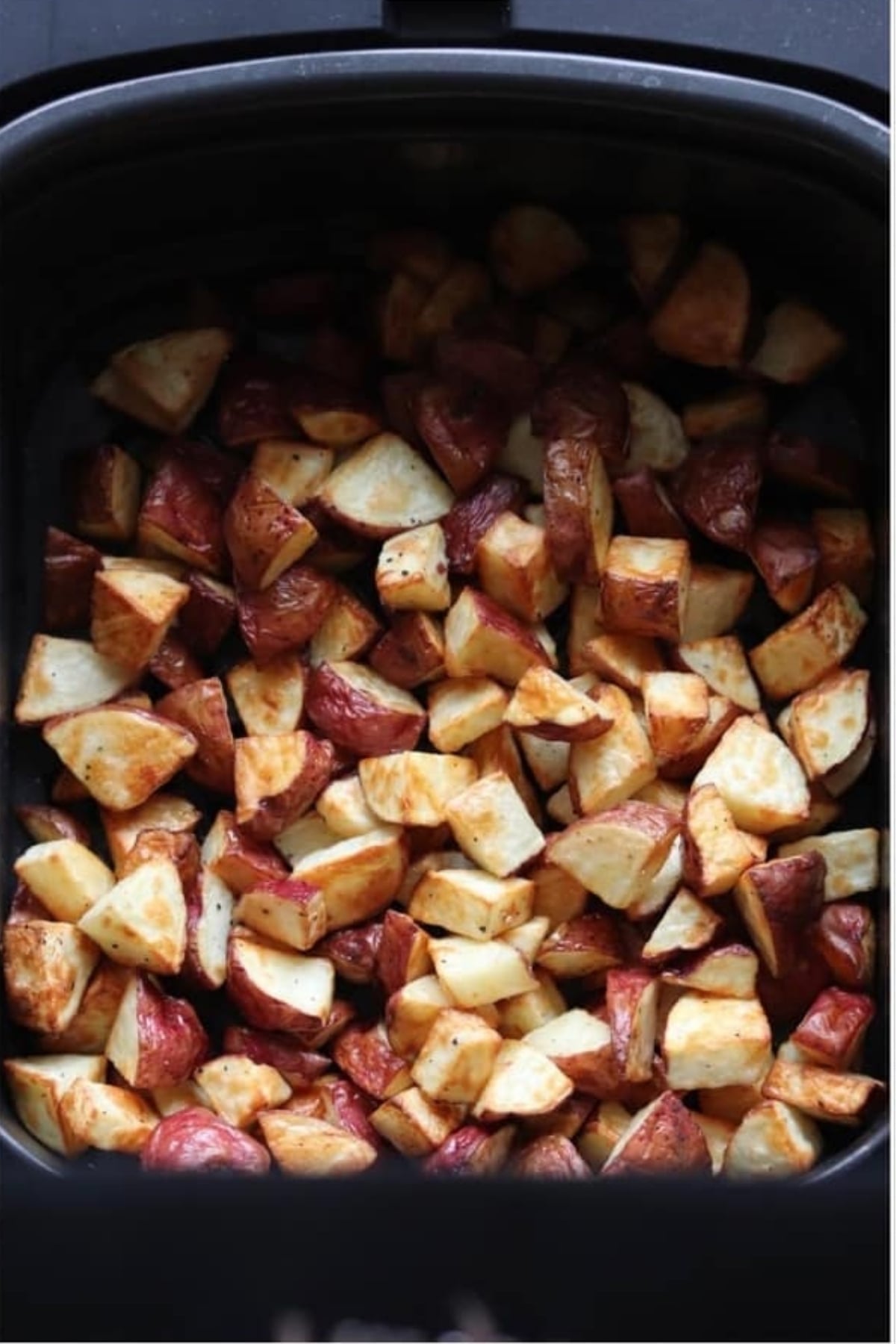 Diced roasted potatoes with skins on are shown cooked and browned in an air fryer basket.