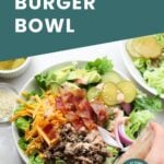 A bowl filled with lettuce, ground beef, shredded cheese, bacon, onions, pickles, and a creamy dressing, with a hand pouring more dressing on top. Text reads "Big Mac Burger Bowl.