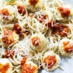 Plate of spaghetti topped with ground chicken meatballs, marinara sauce, and grated cheese, garnished with a basil leaf.