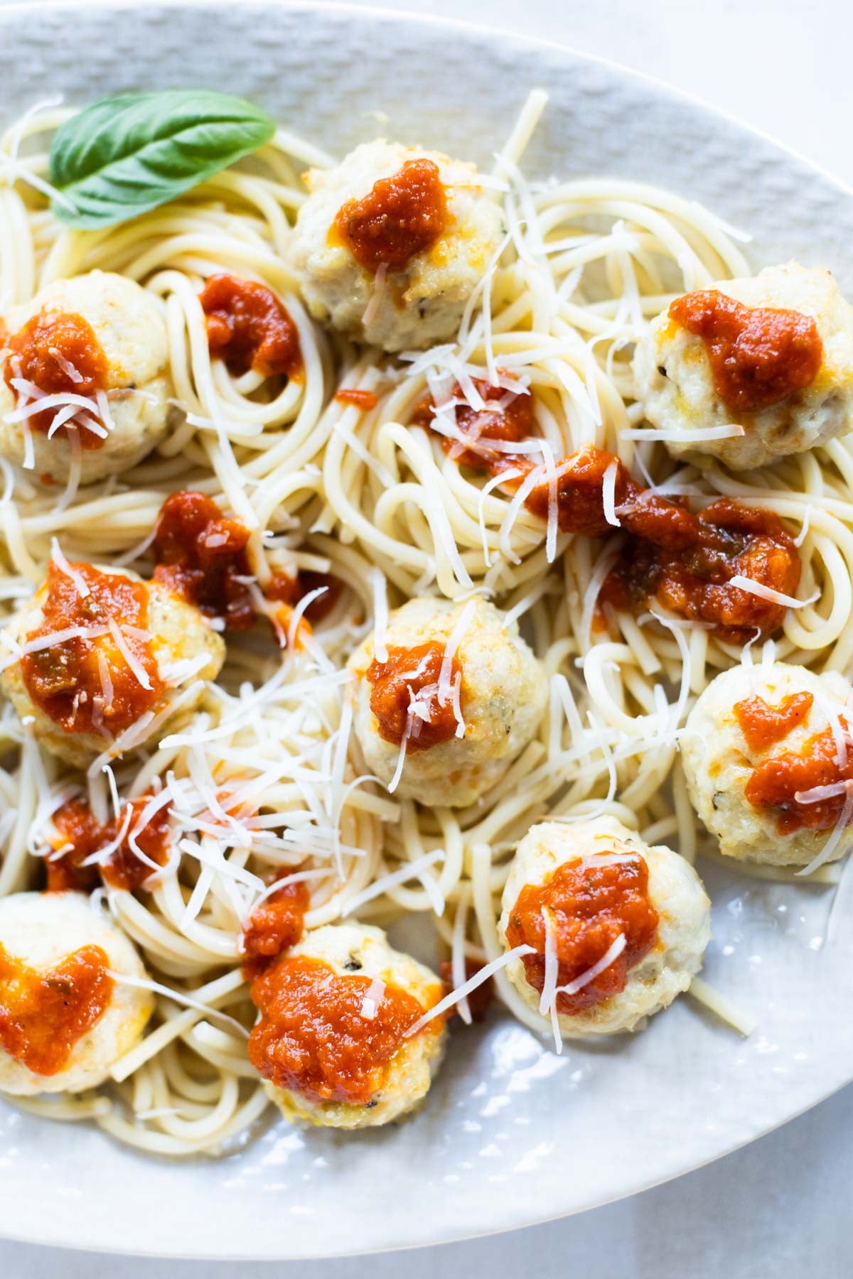 Plate of spaghetti topped with ground chicken meatballs, marinara sauce, and grated cheese, garnished with a basil leaf.