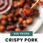 A toothpick holds a piece of crispy pork belly above a plate of pork belly bites, with a dish of sauce in the background. Text reads: "Air Fryer Crispy Pork Belly Bites. cook at home mom.