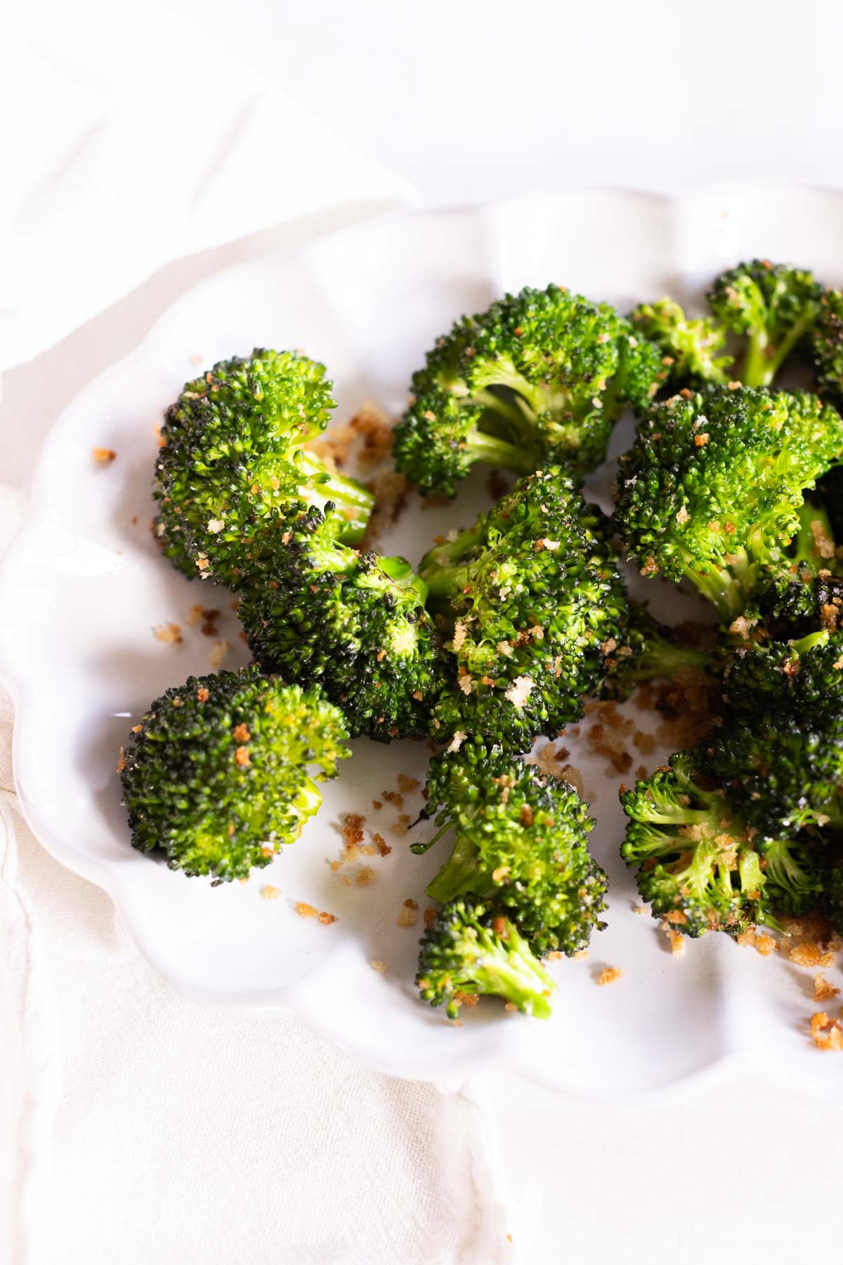Several pieces of sauteed broccoli with browned, crispy edges are arranged on a white plate, sprinkled with parmesan.