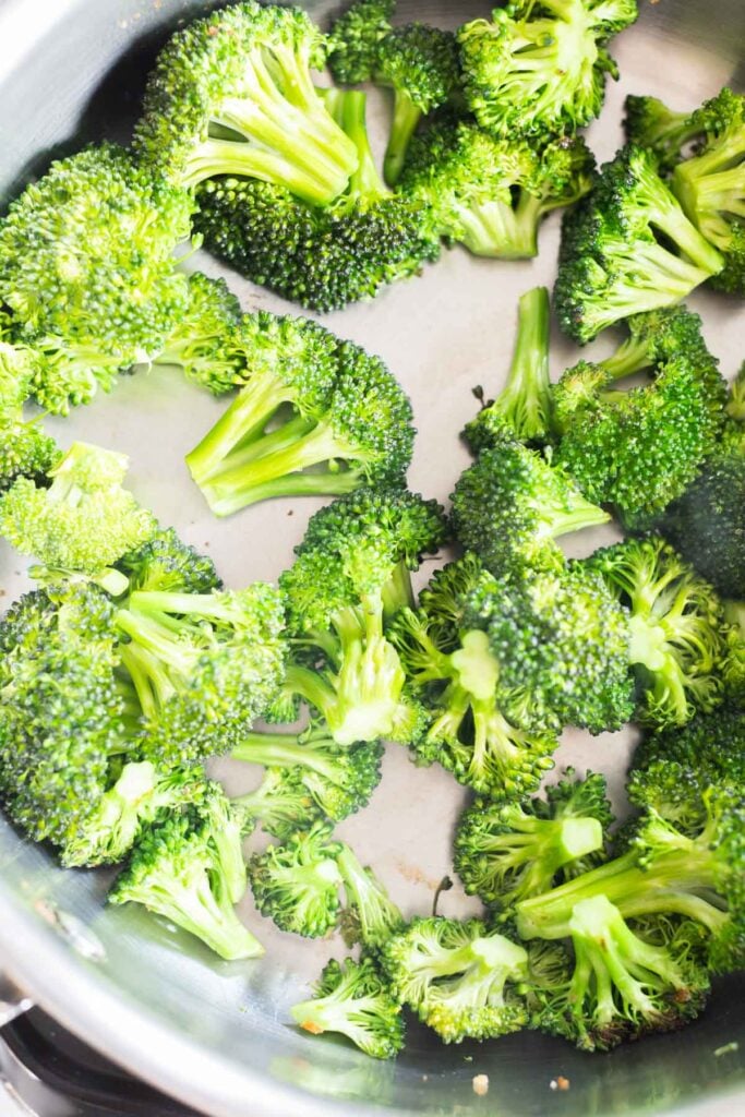 Cooked broccoli florets being in a stainless steel pan.