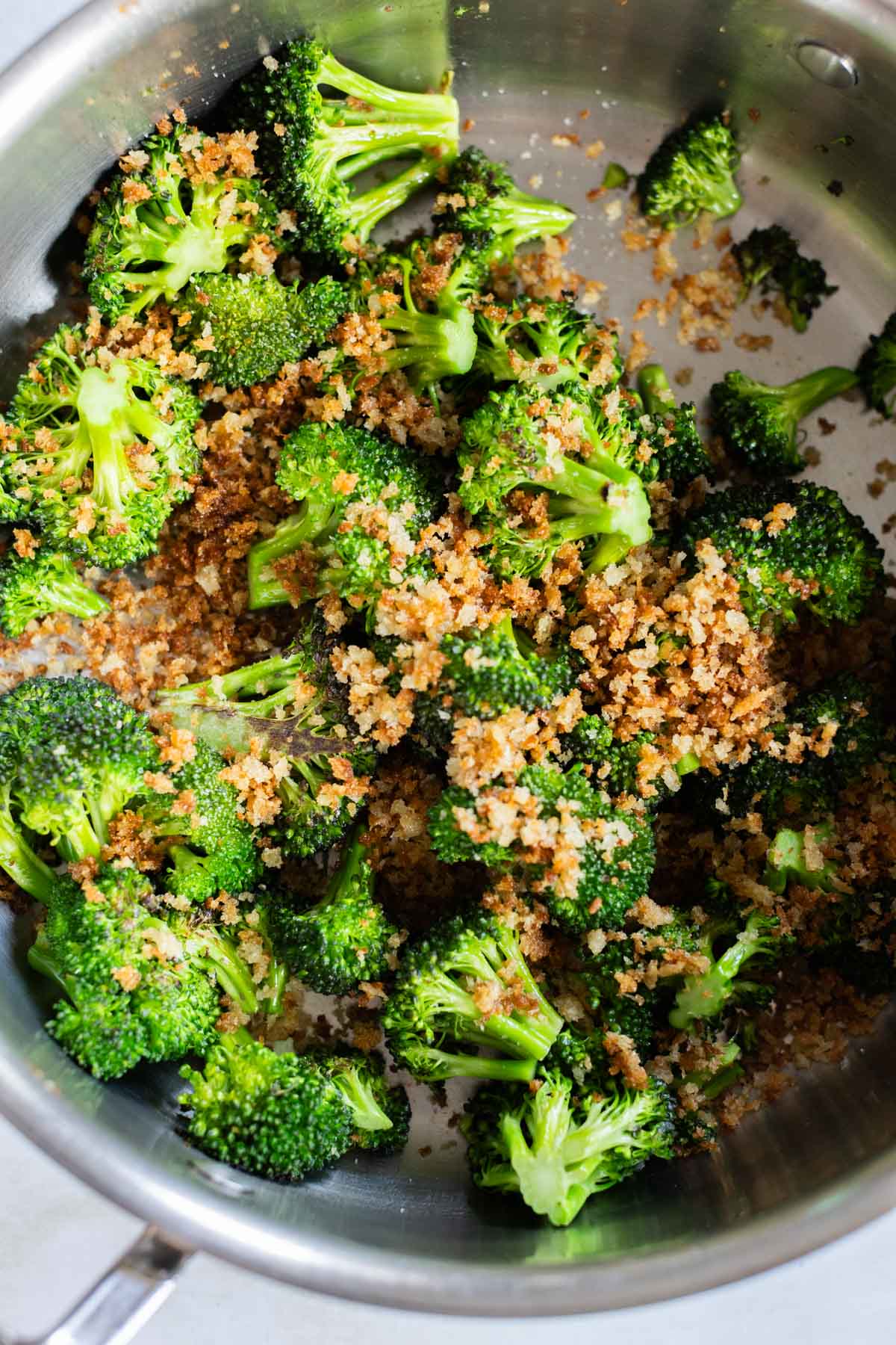 Broccoli florets and toasted parmesan bits in a stainless steel pan.