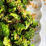 Sauteed parmesan broccoli florets topped on a white scalloped plate.