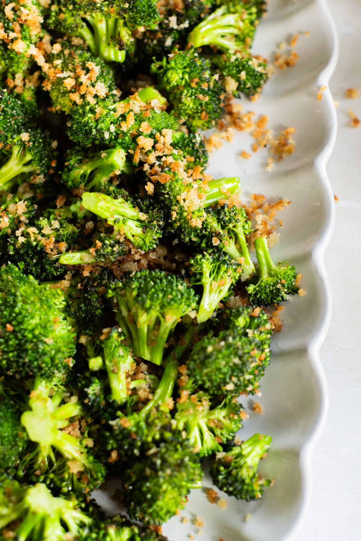 Sauteed parmesan broccoli florets topped on a white scalloped plate.