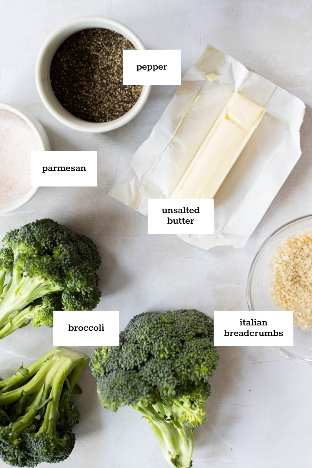 Ingredients on a white surface include broccoli, unsalted butter, pepper, parmesan, and Italian breadcrumbs, each labeled with text.