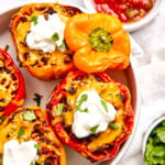 A plate of stuffed bell peppers topped with melted cheese, sour cream, and cilantro, served with a side of salsa.