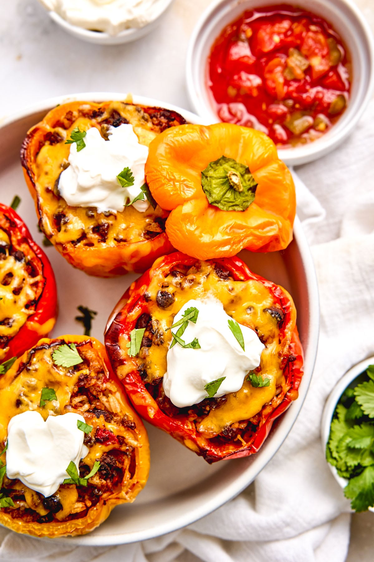 A plate of stuffed bell peppers topped with melted cheese, sour cream, and cilantro, served with a side of salsa.