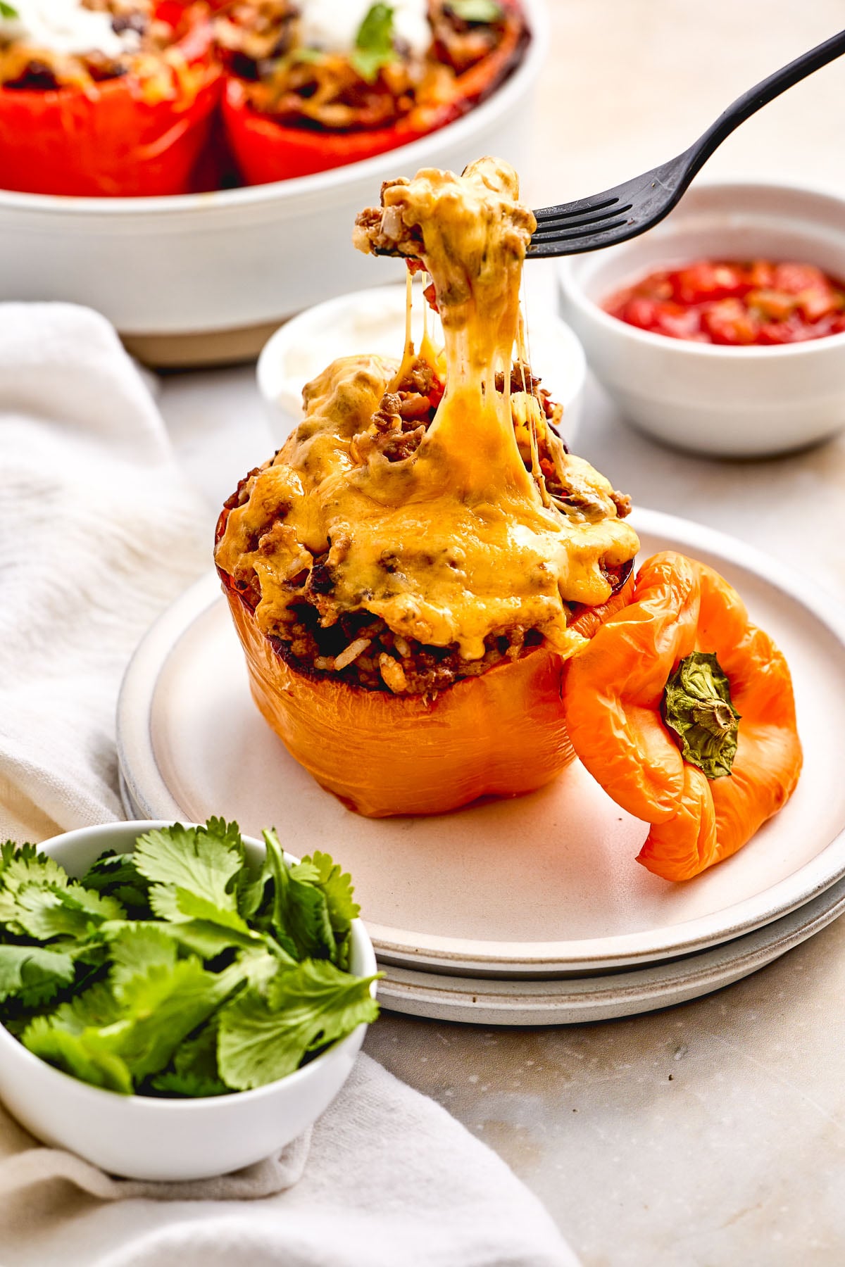 A stuffed pepper with rice topped with melted cheese is being lifted with a fork, served on a plate with a side of cilantro.