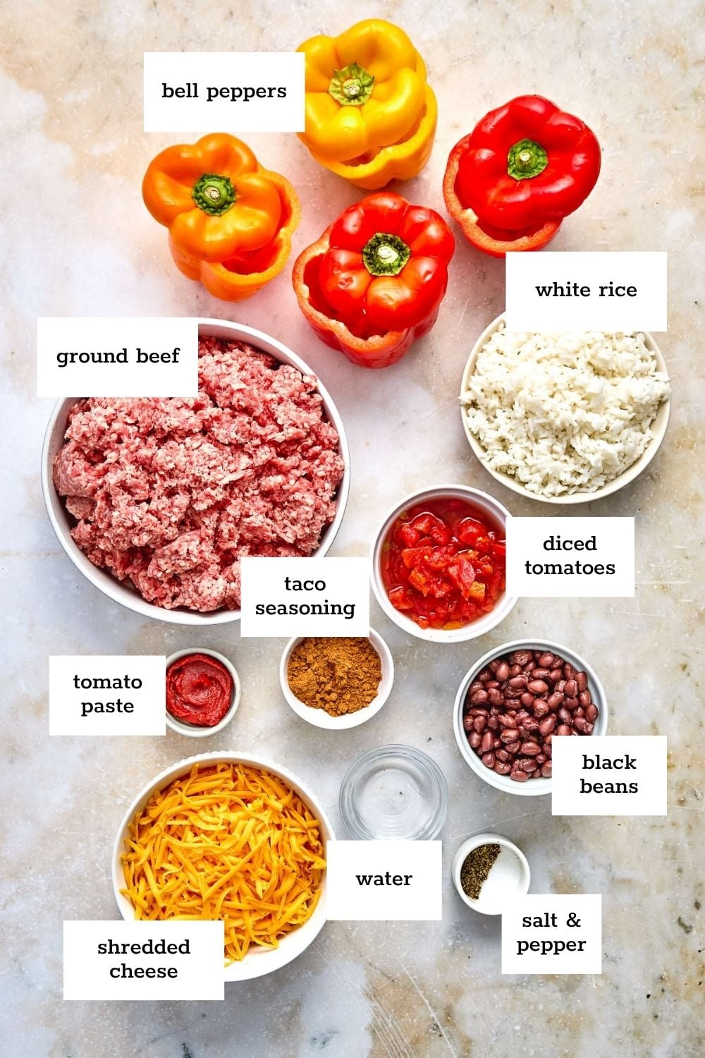 Ingredients for stuffed bell peppers are arranged on a surface, including bell peppers, ground beef, rice, diced tomatoes, black beans, cheese, tomato paste, taco seasoning, water, and seasonings.