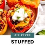 A plate of stuffed bell peppers filled with a meat and rice mixture, topped with melted cheese, sour cream, and cilantro. The text reads: "Air Fryer Stuffed Peppers cook at home mom.