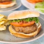A ground turkey burger served on a bun with lettuce and tomato on a plate with potato chips.