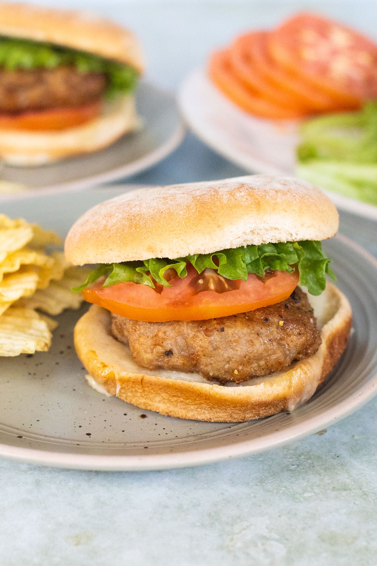 A ground turkey burger served on a bun with lettuce and tomato on a plate with potato chips.