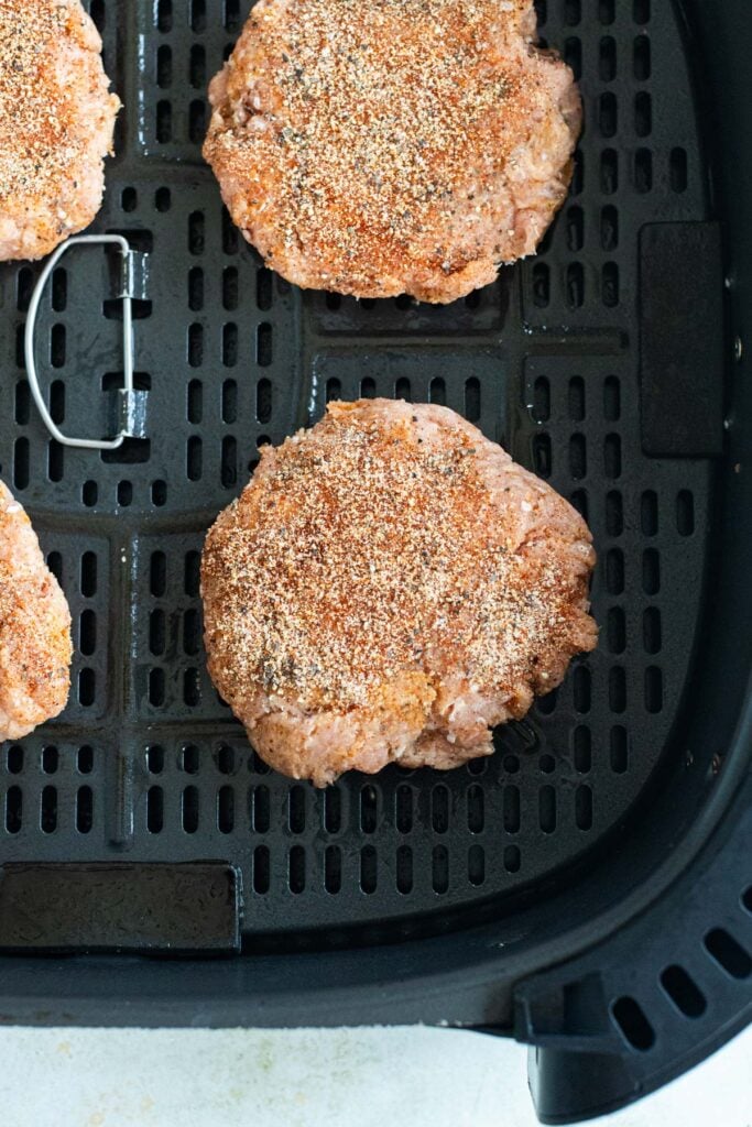 Uncooked turkey burgers in air fryer basket, ready to be cooked.