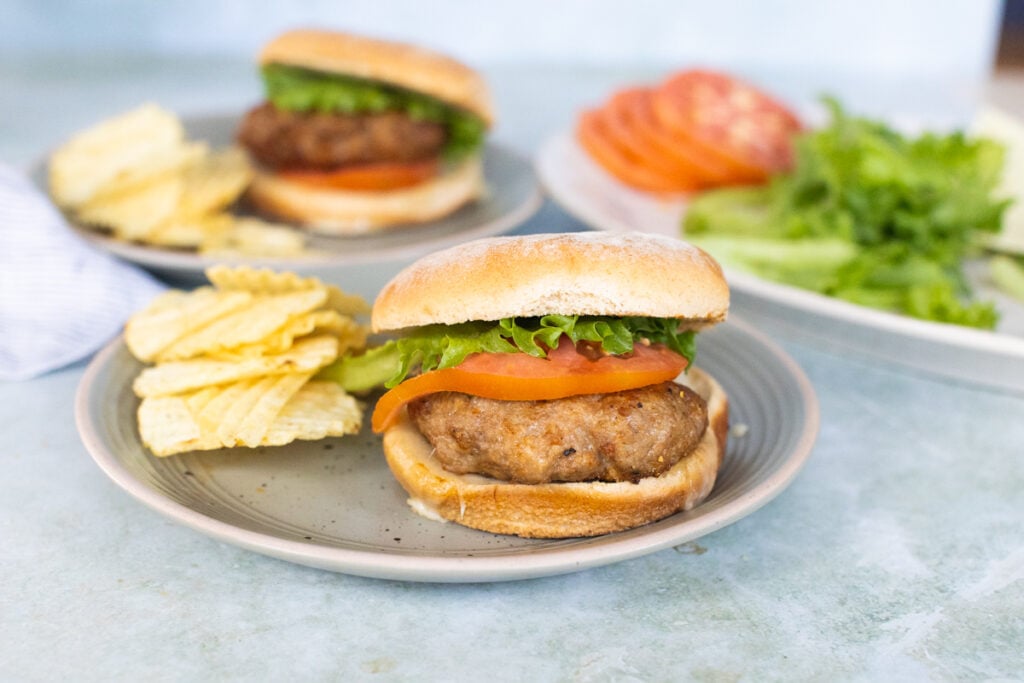 Turkey burger with lettuce and tomato, served won a hamburger bun, plated with potato chips.