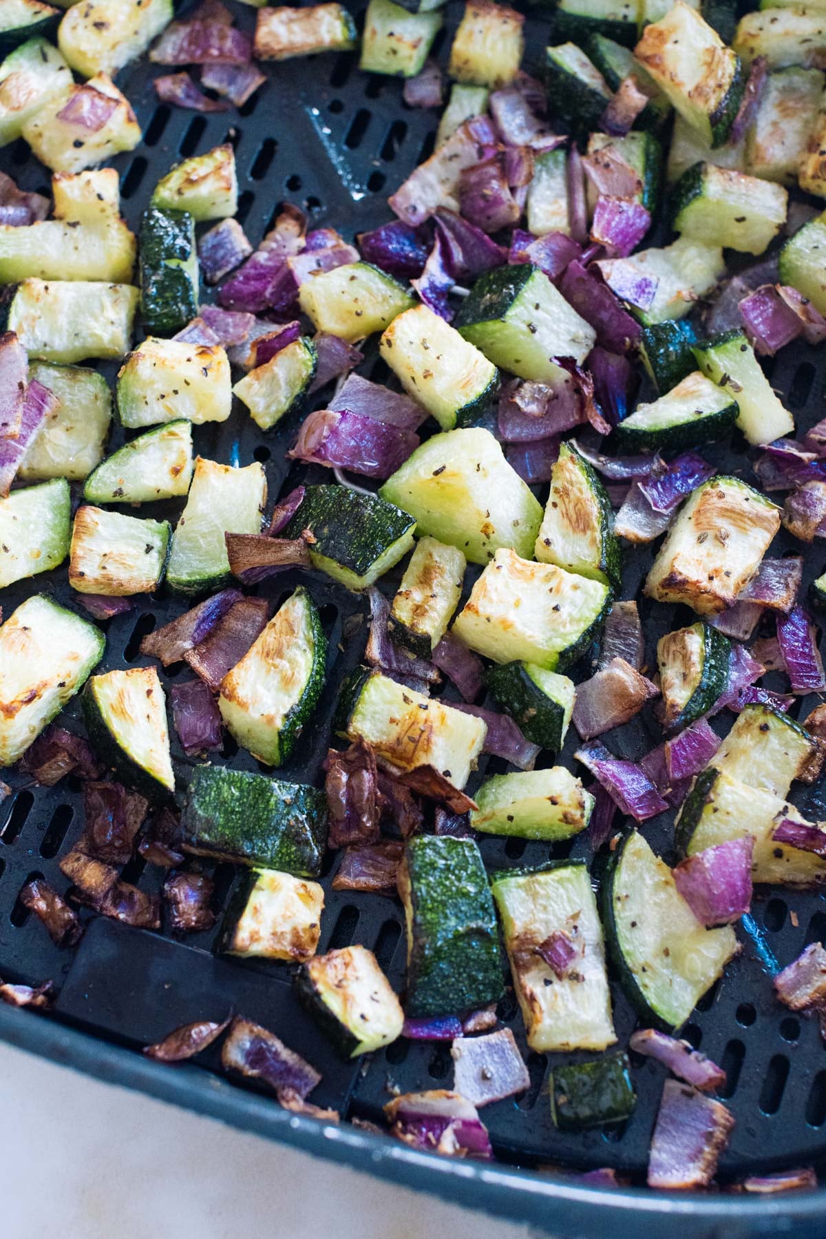Chopped zucchini and red onions are roasted and lightly browned in an air fryer basket.